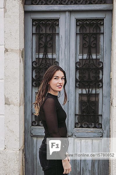 Porträt einer lächelnden brünetten jungen Frau  die vor einer alten Tür steht
