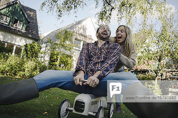 Lachendes Paar  das vorgibt  im Garten ein Spielzeugauto zu fahren