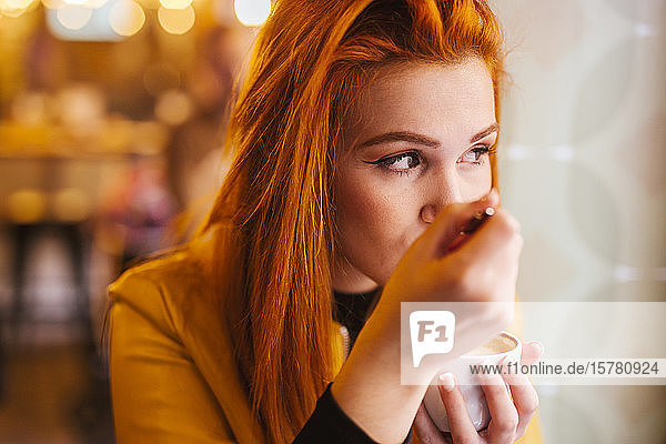 Porträt einer rothaarigen jungen Frau  die in einem Café Cappuccino trinkt