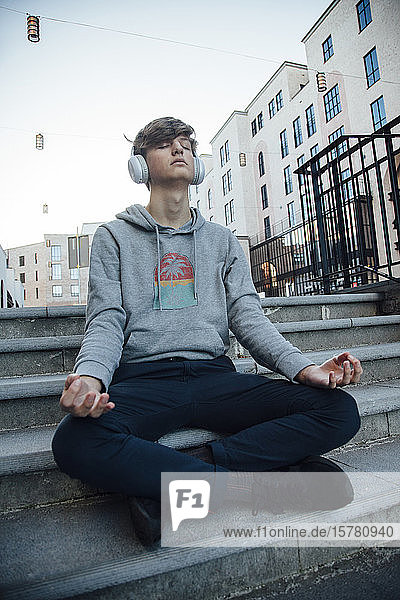 Teenager sitzt auf Stufen  meditiert in der Stadt und hört Musik