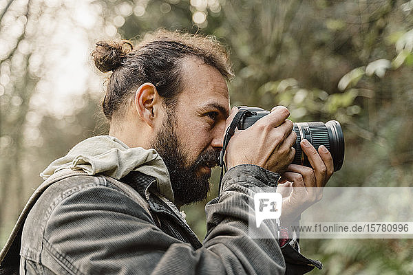 Junger Mann fotografiert im Wald mit seiner Kamera