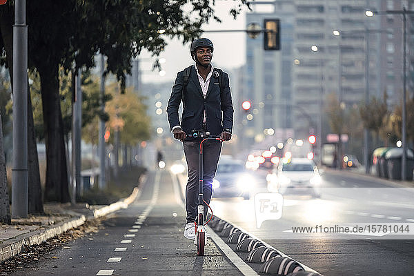 Porträt eines Geschäftsmannes  der abends auf einem Roller auf dem Fahrradweg fährt