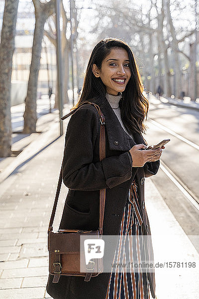 Portrait of smiling young woman with smartphone at the tram stop