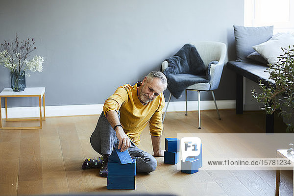 Mature man playing with building blocks on the floor at home