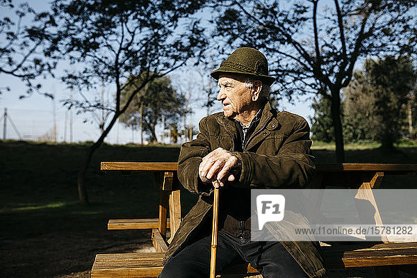 Old man with cane sitting on banch in a park