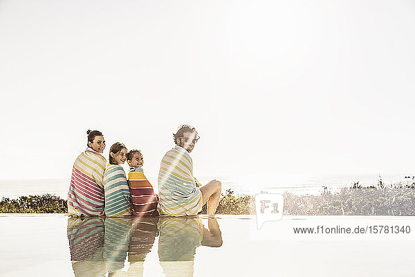 In Handtücher gewickelte Familie sitzt bei Sonnenuntergang am Pool