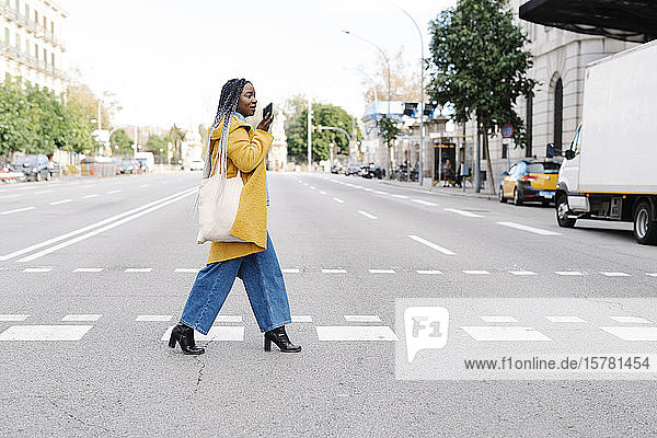Junge Frau überquert die Straße mit dem Handy  Barcelona  Spanien