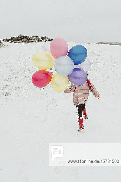 Rückenansicht eines Mädchens mit Ballons  das im Winter einen Hügel hinaufläuft