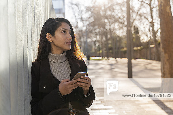 Young woman with smartphone in the city looking around