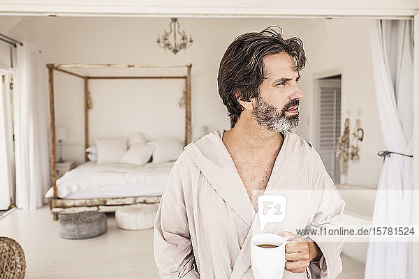 Mann im Bademantel mit einer Tasse Kaffee im Schlafzimmer