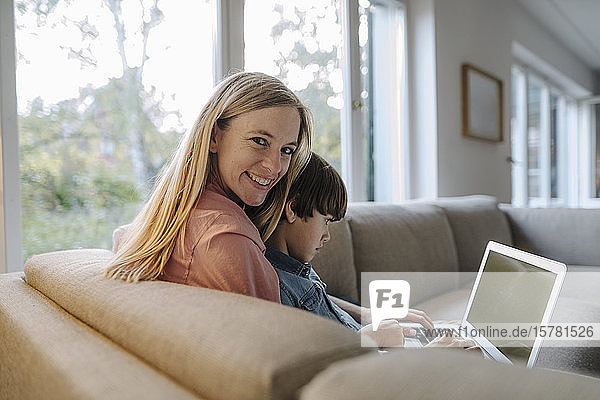 Mother and son sitting on couch  using laptop