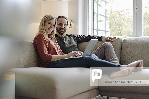 Couple sitting at home on couch  using laptop