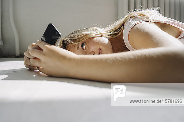 Blonde junge Frau liegt auf dem Boden und benutzt ihr Handy