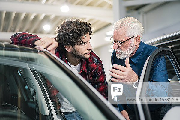 Autohändler zeigt Auto einem jungen Mann im Ausstellungsraum