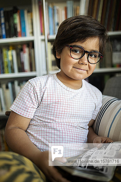 Portrait of smiling boy with glasses reading comic at home