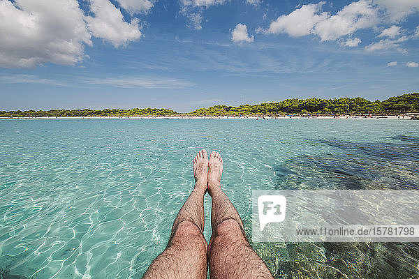 Die Beine eines Mannes vor dem Strand von Son Saura  Menorca  Spanien.