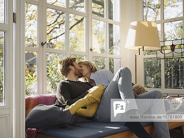 Paar küsst sich zu Hause im Wintergarten  während der Sohn auf dem Schoß liegt