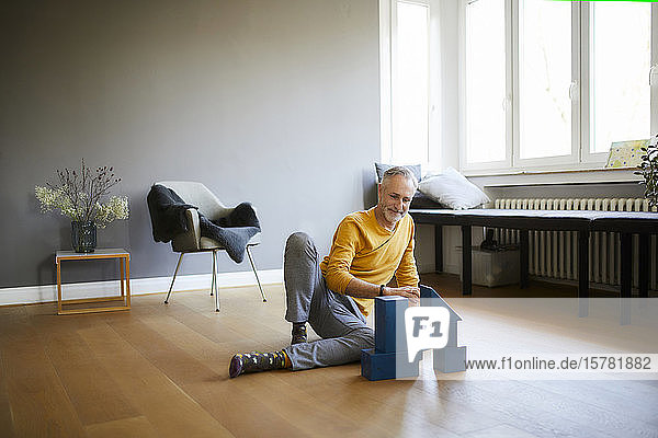 Reifer Mann spielt zu Hause mit Bauklötzen auf dem Boden