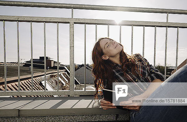 Rothaarige Frau mit Tablette entspannt auf der Dachterrasse