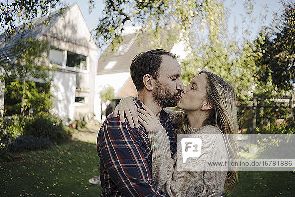 Glückliches Paar küsst sich im Garten  vor ihrem Traumhaus