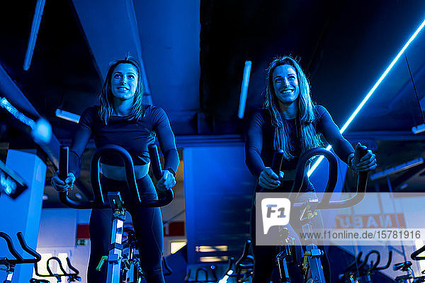 Lächelnde Zwillingsschwestern trainieren auf Spinning-Bikes in der Turnhalle