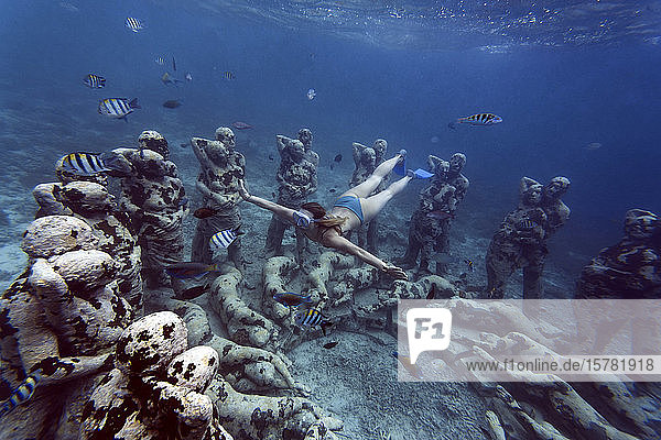 Woman swimming near underwater sculpture made by Jason deCaires Taylor Gili Meno island Bali Indonesia