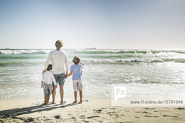 Vater geht mit seinen Söhnen am Strand spazieren und beobachtet das Meer