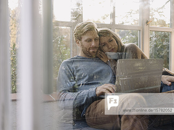 Mann und Frau benutzen zu Hause einen Laptop im Wintergarten