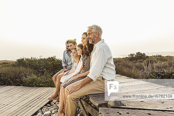Große Familie genießt den Sonnenuntergang auf einer Strandpromenade sitzend