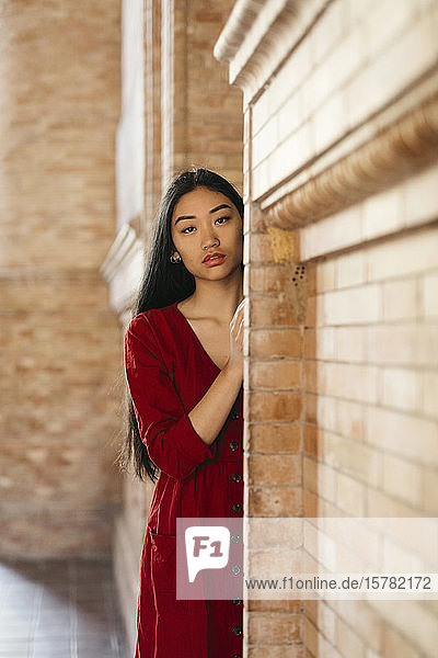 Porträt einer schönen jungen Frau in einem roten Kleid an einer Ziegelmauer