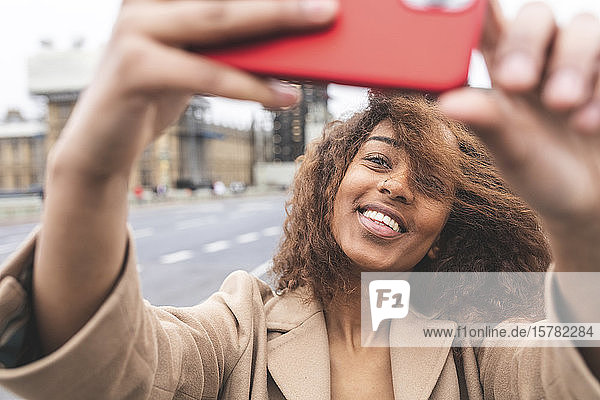 Lächelnde junge Frau  die in der Stadt mit Big Ben im Hintergrund ein Selfie macht  London  Großbritannien