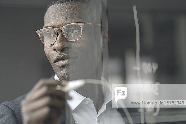 Portrait of content young businessman drawing diagram on glass pane