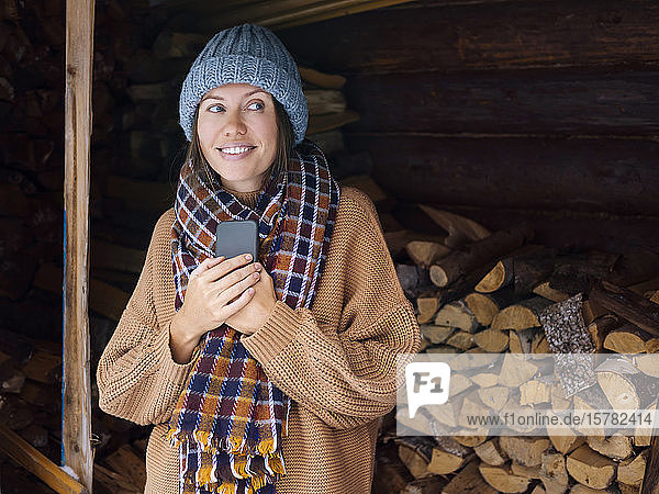 Junge Frau in der Nähe eines Holzstapels mit einem Smartphone