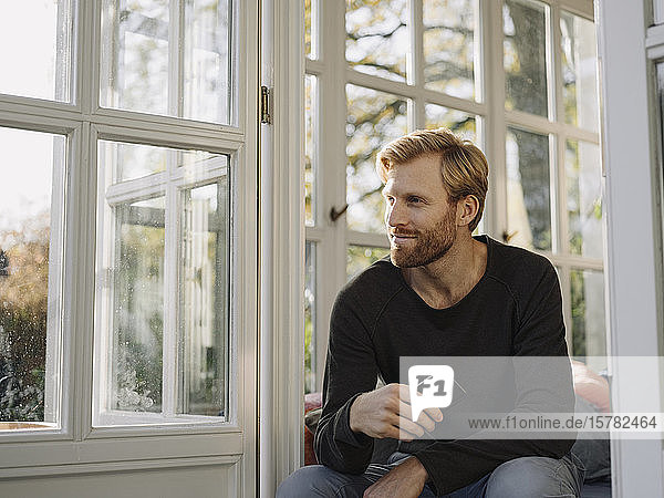 Mann sitzt zu Hause im Wintergarten