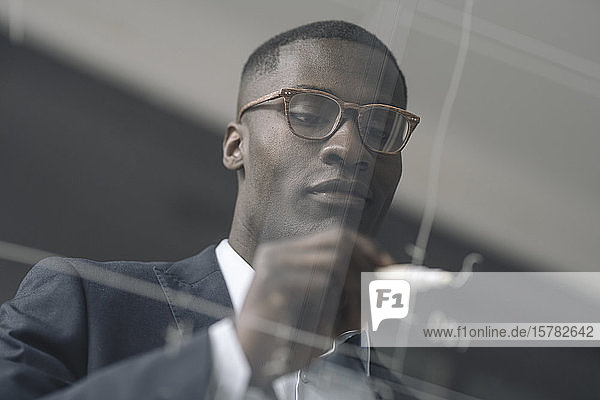 Portrait of young businessman drawing diagram on glass pane in office