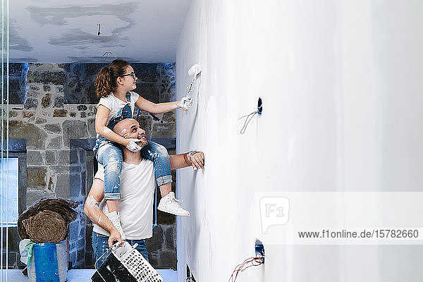 Girl sitting on father's shoulders painting the wall of her new house