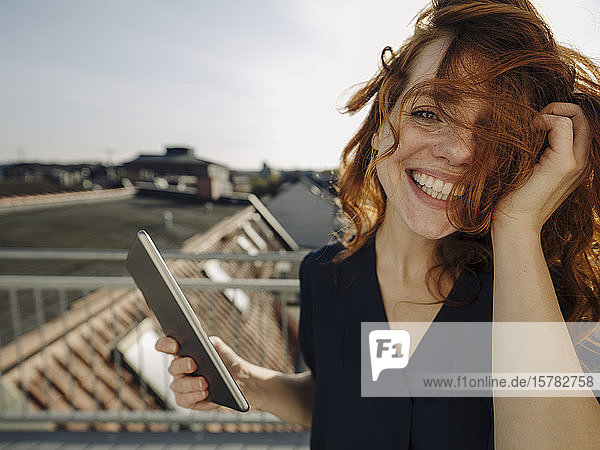 Portrait of happy redheaded woman with tablet on rooftop terrace