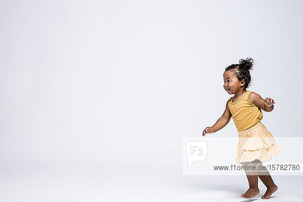 Happy little girl running barefoot in front of grey background