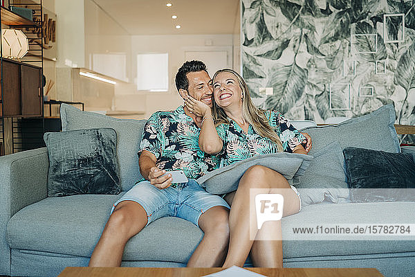 Glückliches Paar sitzt auf der Couch im Wohnzimmer und trägt hawaiianische Hemden