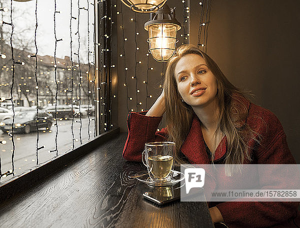 Porträt einer entspannten jungen Frau in einem Café  die aus dem Fenster schaut