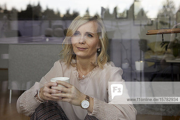 Porträt einer blonden Frau hinter einer Fensterscheibe zu Hause