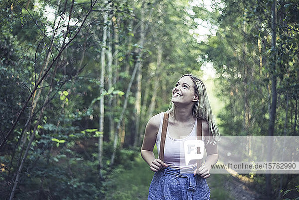 Porträt einer lächelnden jungen Frau mit Rucksack im Wald  die etwas beobachtet