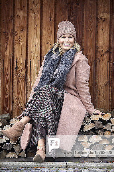 Portrait of smiling woman in winter clothes sitting on stack of wood