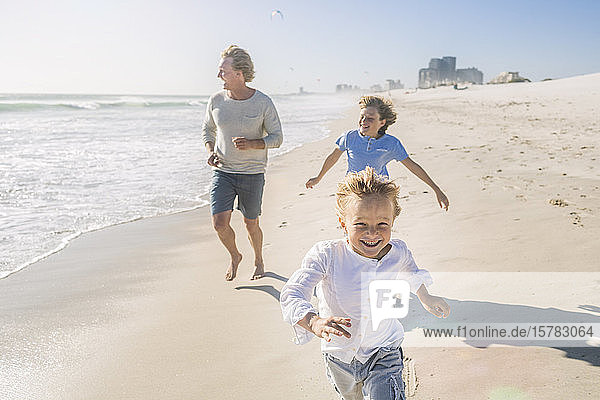 Father having fun with his sons on the beach  running and jumping in the sand