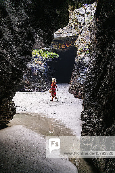 Blond woman wearing red dress and hat at a rock cave  Playa de Las Catedrales  Spain