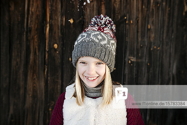 Portrait of happy girl wearing woolly hat at wooden wall