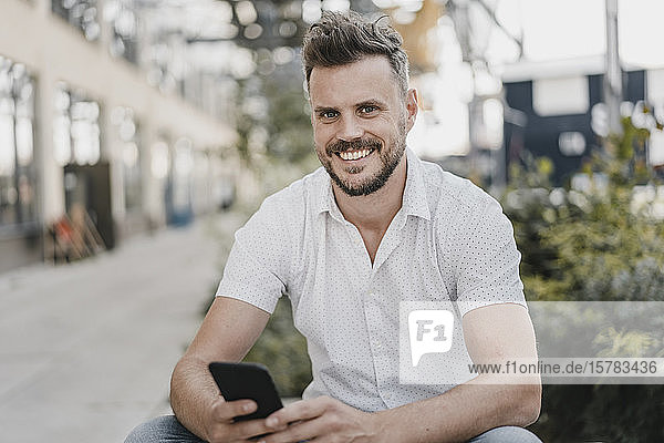Young smiling man using smartphone and looking at camera