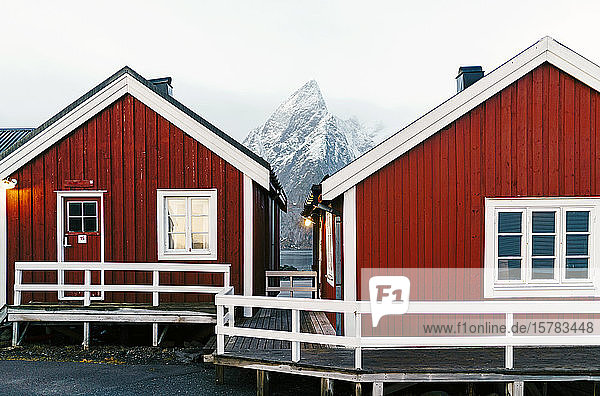 Rote Hütten und schneebedeckter Berg an der Küste Hamnoy Lofoten Norwegen