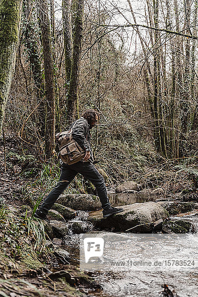 young man with backpack  crossing steam in forest