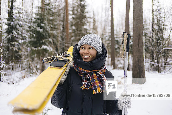Porträt einer lächelnden Frau mit Skiern im Winterwald